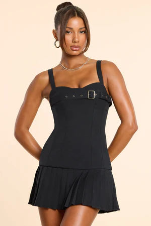 Black sleeveless mini dress with silver buckle bust detail and pleated drop-hem skirt — close-up